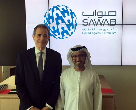 Two men standing in front of a display wall showing the Sawab Center logo, with English and Arabic text.