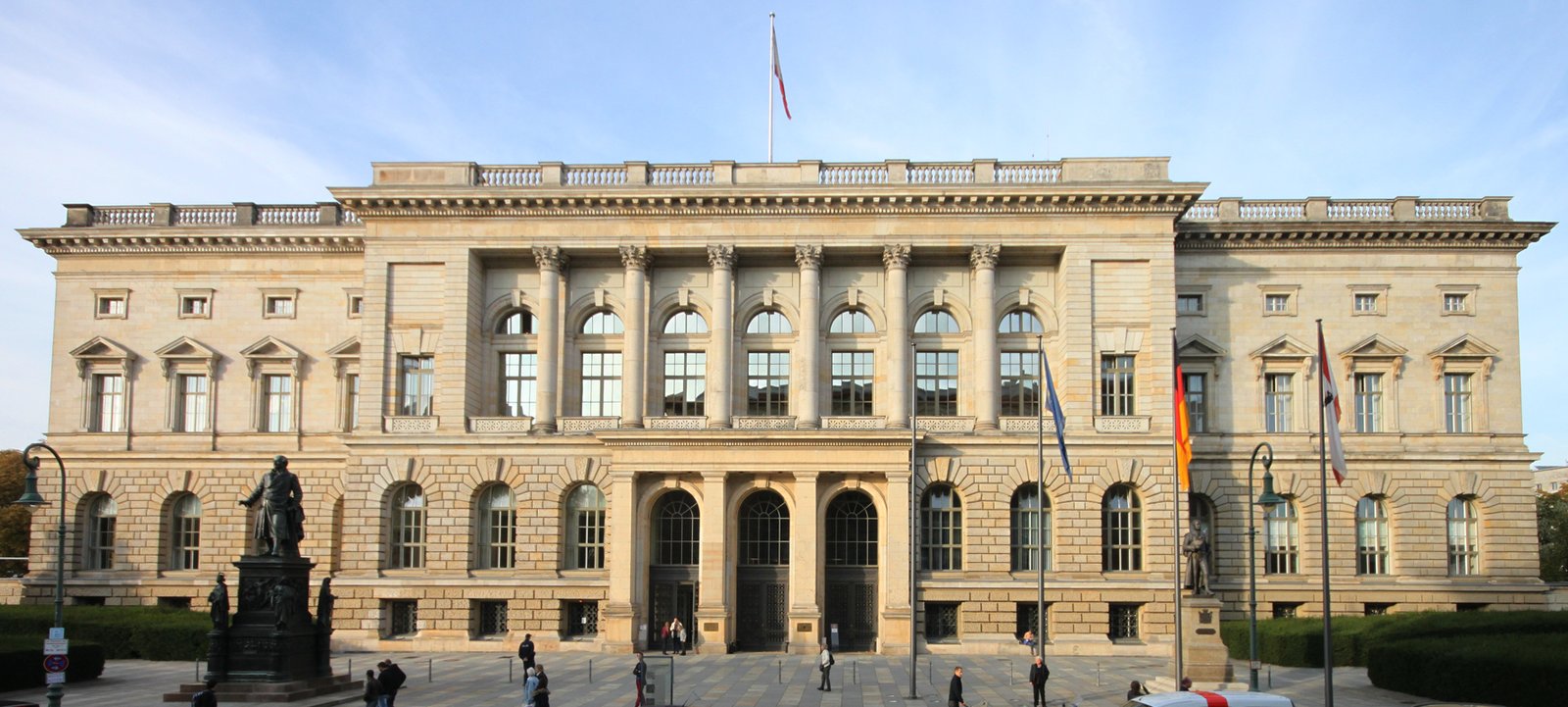 Front facade of the Abgeordnetenhaus of Berlin on Niederkirchnerstrasse, with European Union, German and Berlin flags in front and a few pedestrians on the forecourt