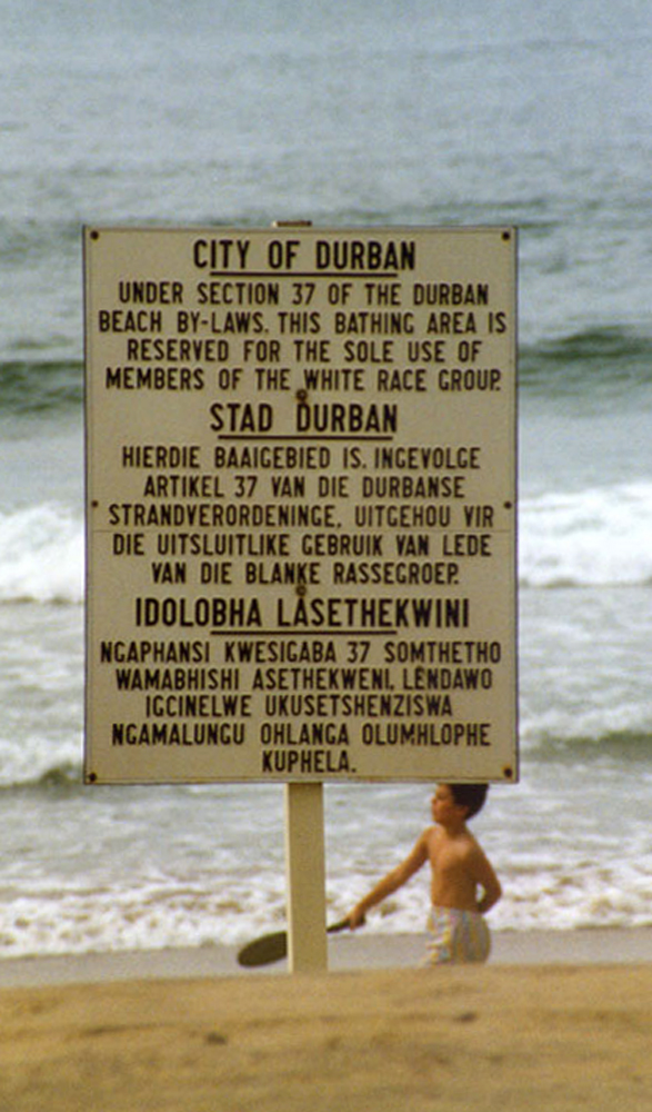 Beach sign in Durban, 1989, in English, Afrikaans and Zulu: "City of Durban. Under section 37 of the Durban beach by-laws, this bathing area is reserved for the sole use of members of the white race group."