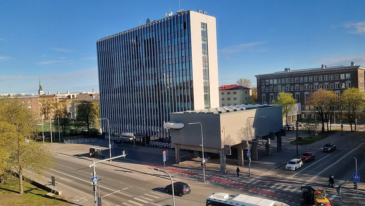 A tall glass-fronted office block with a concrete annex, seen from above across a street junction in Tallinn