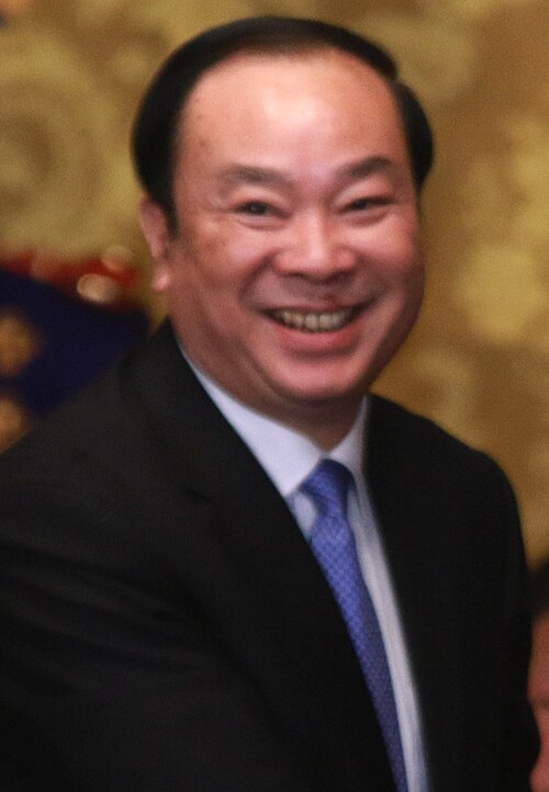 Portrait photograph of Huang Kunming, smiling, in a dark suit and blue tie