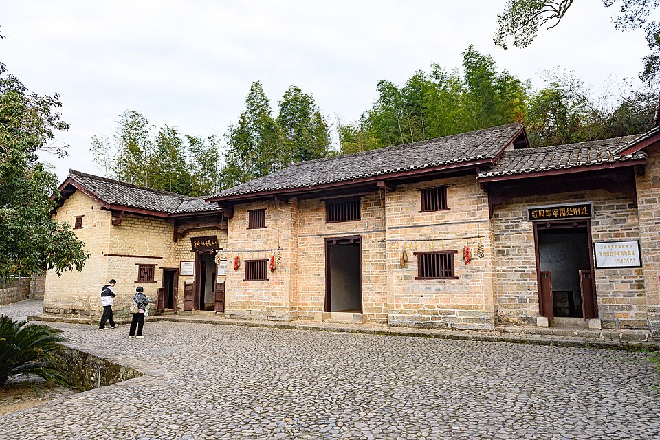 Two-storey brick and tile farmhouse buildings with signboards on a cobbled courtyard at Maoping, Jinggangshan, two visitors walking past