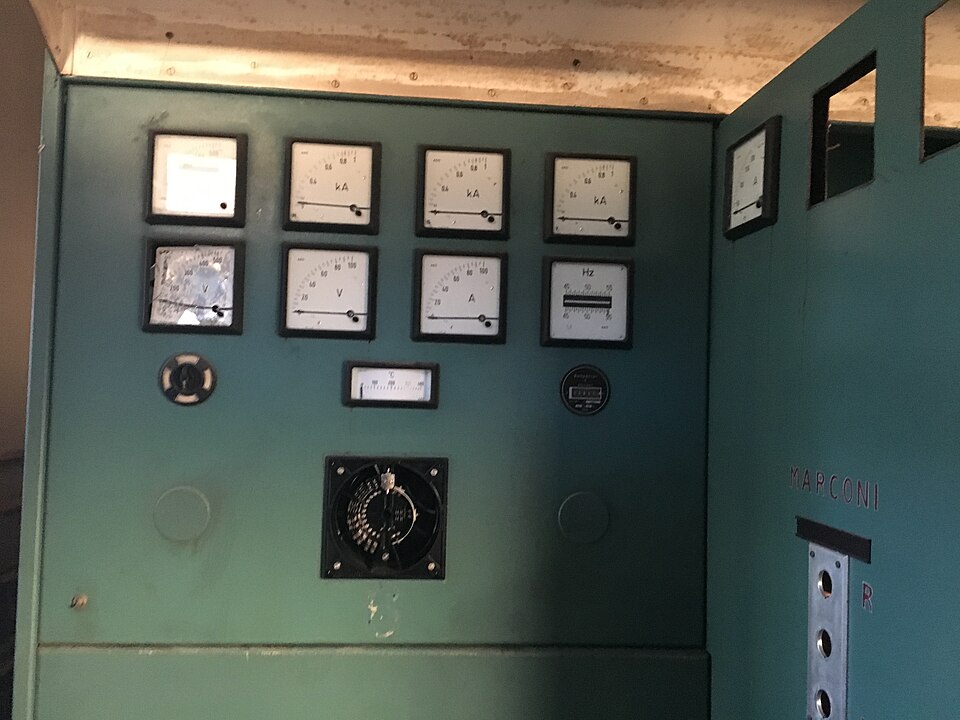 Green equipment cabinet with analogue current, voltage and frequency meters, inside the abandoned Radio Liberty station at Pals; the word Marconi is stamped on the panel at right