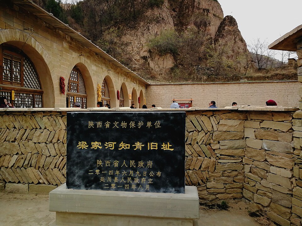 Black plaque with gold characters reading Liangjiahe zhiqing former site, in front of arched cave dwellings
