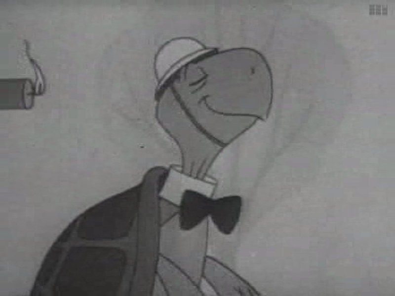 Frame from Duck and Cover: Bert the Turtle, an animated turtle in a hard hat and bow tie, smiling, with a lit firecracker hanging at the left edge