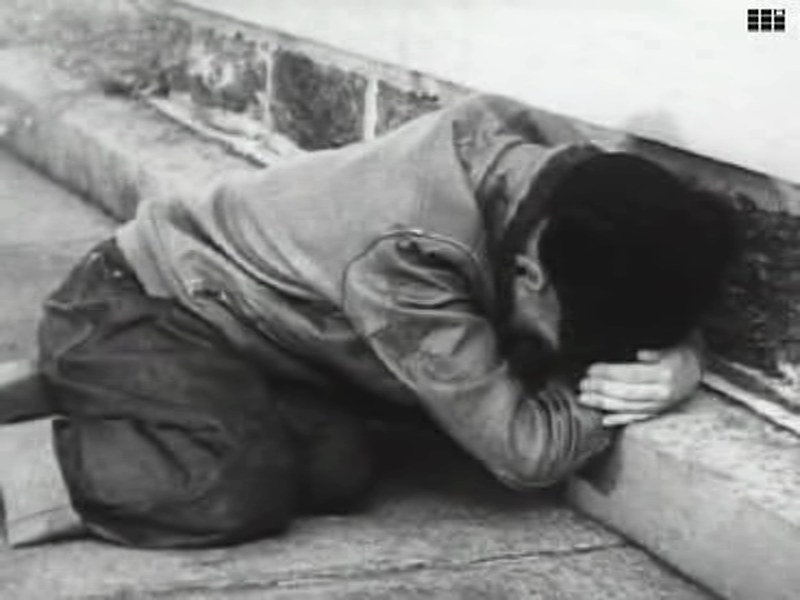 Frame from Duck and Cover: a boy crouches against a low wall with his arms over the back of his head