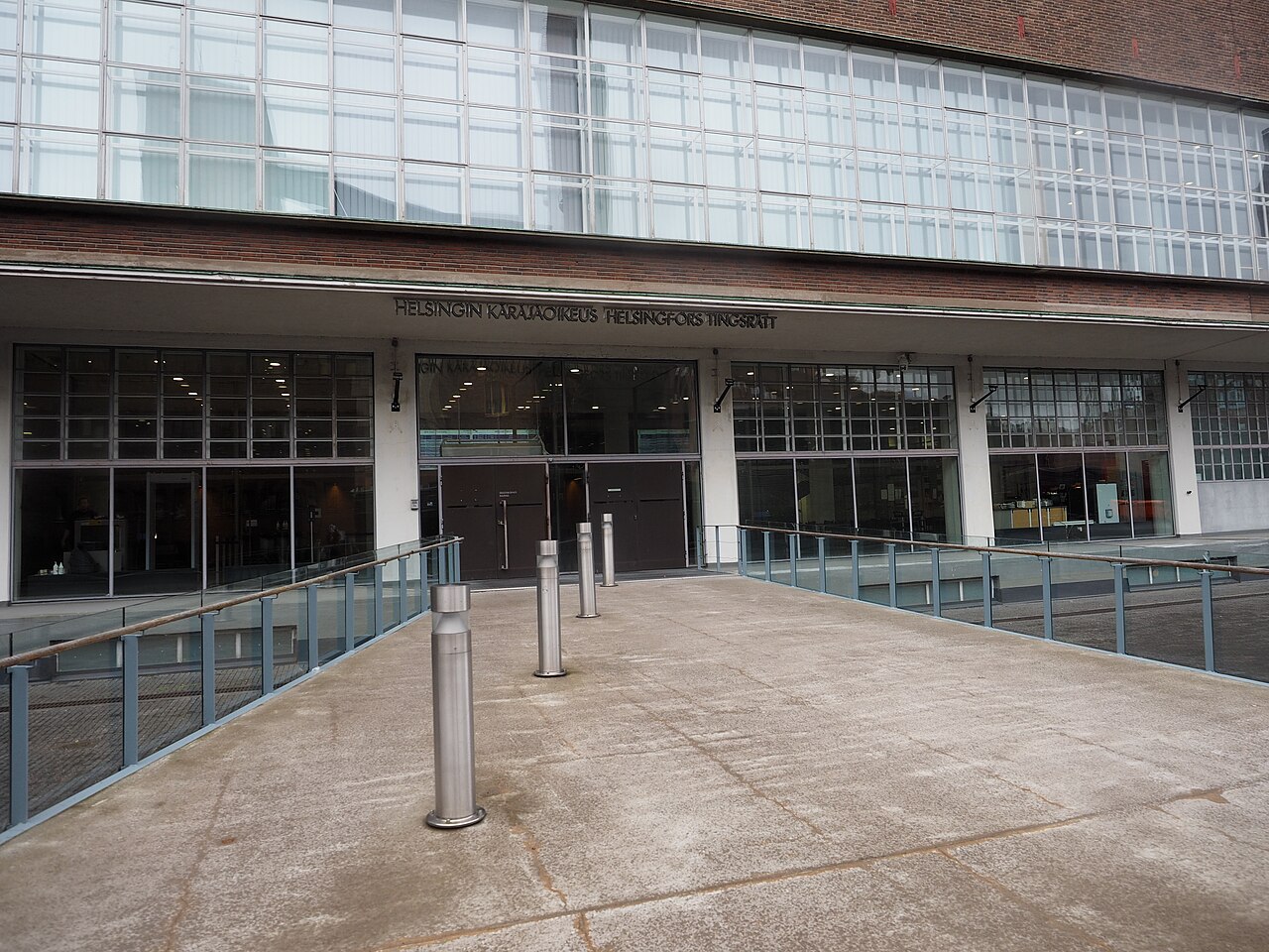 Glass and brick facade with the words Helsingin käräjäoikeus Helsingfors tingsrätt above a ramp and entrance doors