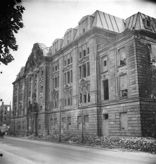 The same building in ruins, with empty window openings and rubble along the pavement, Berlin, June 1949
