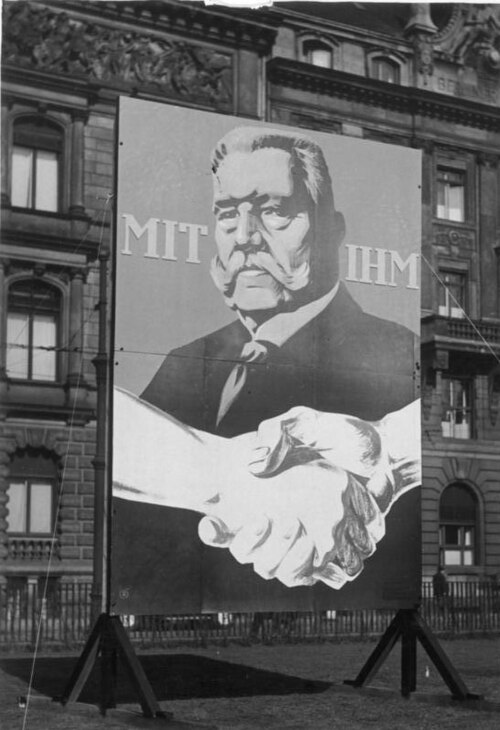 Photograph of a large hoarding in Berlin showing a portrait of Paul von Hindenburg above a handshake, with the words "Mit ihm" (With him) either side of his face