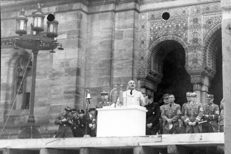 Julius Streicher speaking at a podium in front of the Nuremberg synagogue before its demolition, 10 August 1938
