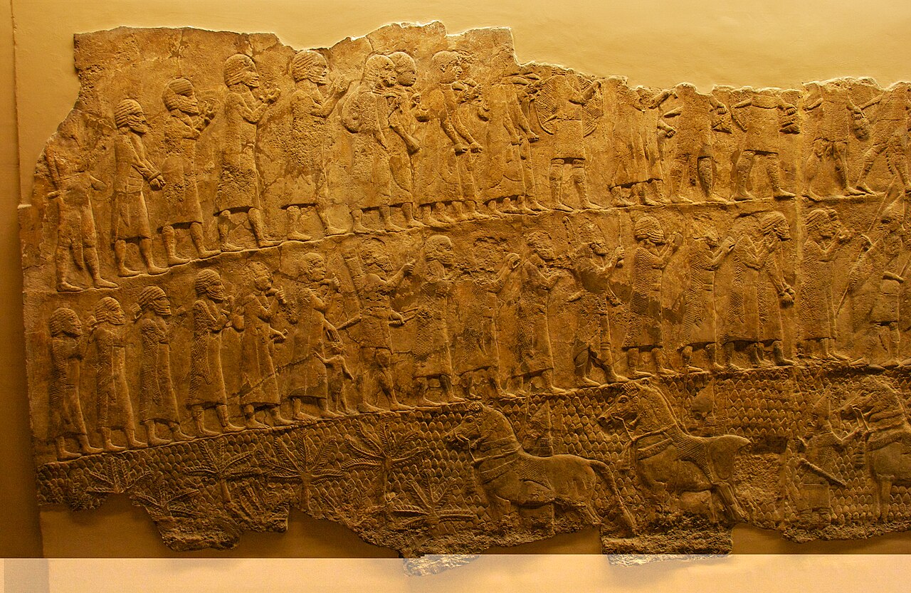 Assyrian relief from Nineveh: rows of deportees with bundles walk out of Lachish, with horses below
