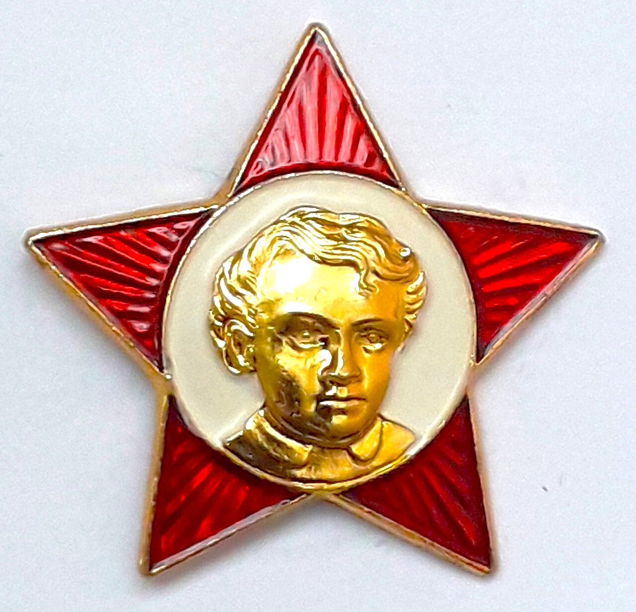 Photograph of a second Little Octobrist badge design: a gold-toned enamelled red star with a relief profile of young Lenin's face in its centre, rather than the photographic portrait used on the plastic version