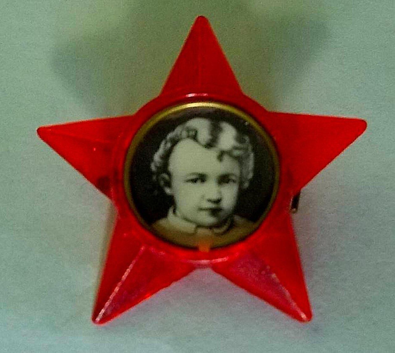 Photograph of a Little Octobrist badge: a red plastic five-pointed star with a circular black-and-white photographic portrait of Lenin as a small curly-haired child set in its centre