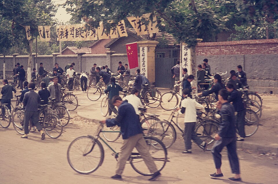 Crowd with bicycles outside a gateway under banners, China, September 1976