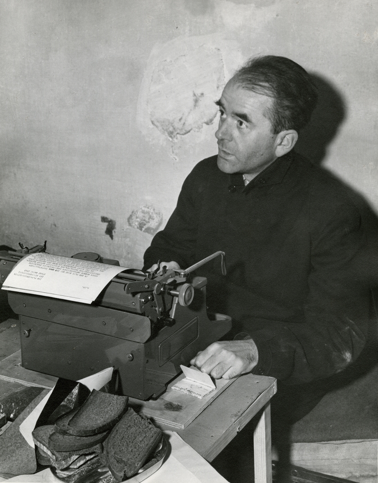 Albert Speer seated at a typewriter in his cell at Nuremberg, a plate of bread in the foreground