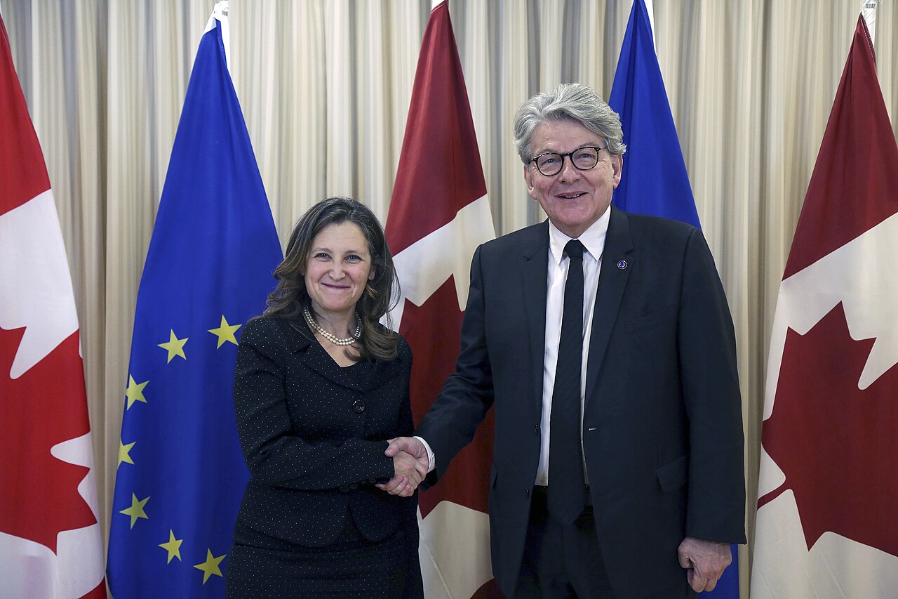 Thierry Breton, European Commissioner for Internal Market, shaking hands with Canada's Chrystia Freeland in front of EU and Canadian flags