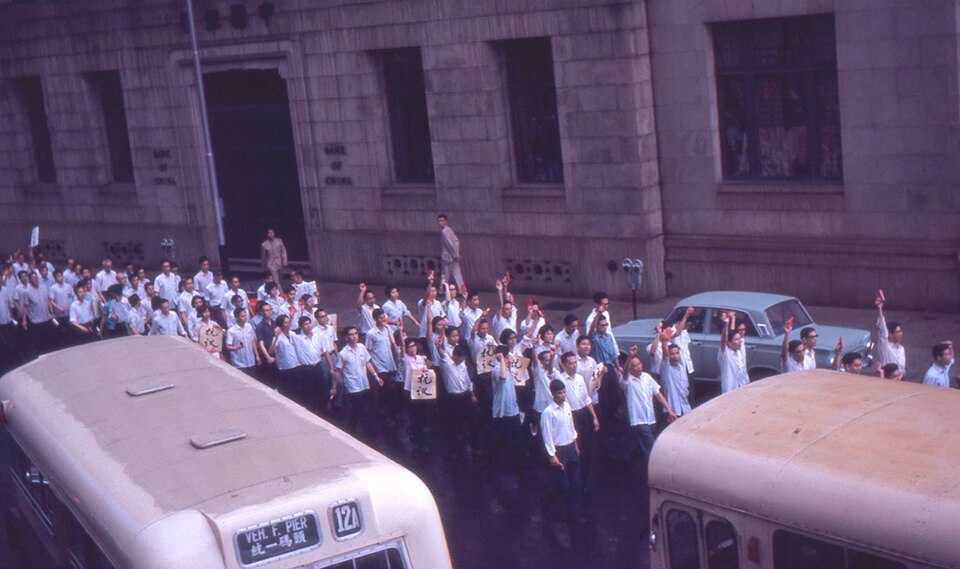Column of demonstrators in Hong Kong in May 1967 raising small red books beside the Bank of China building