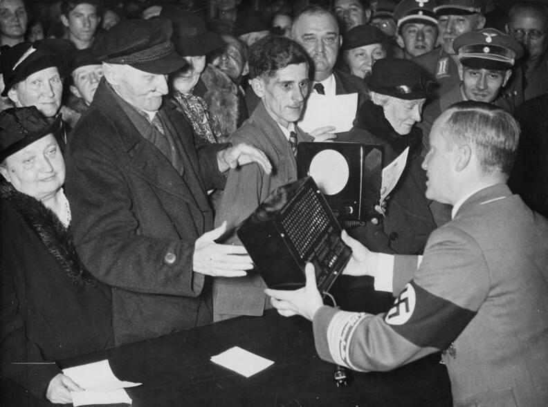 Crowd receiving small radio sets from a uniformed party official in Berlin, October 1938