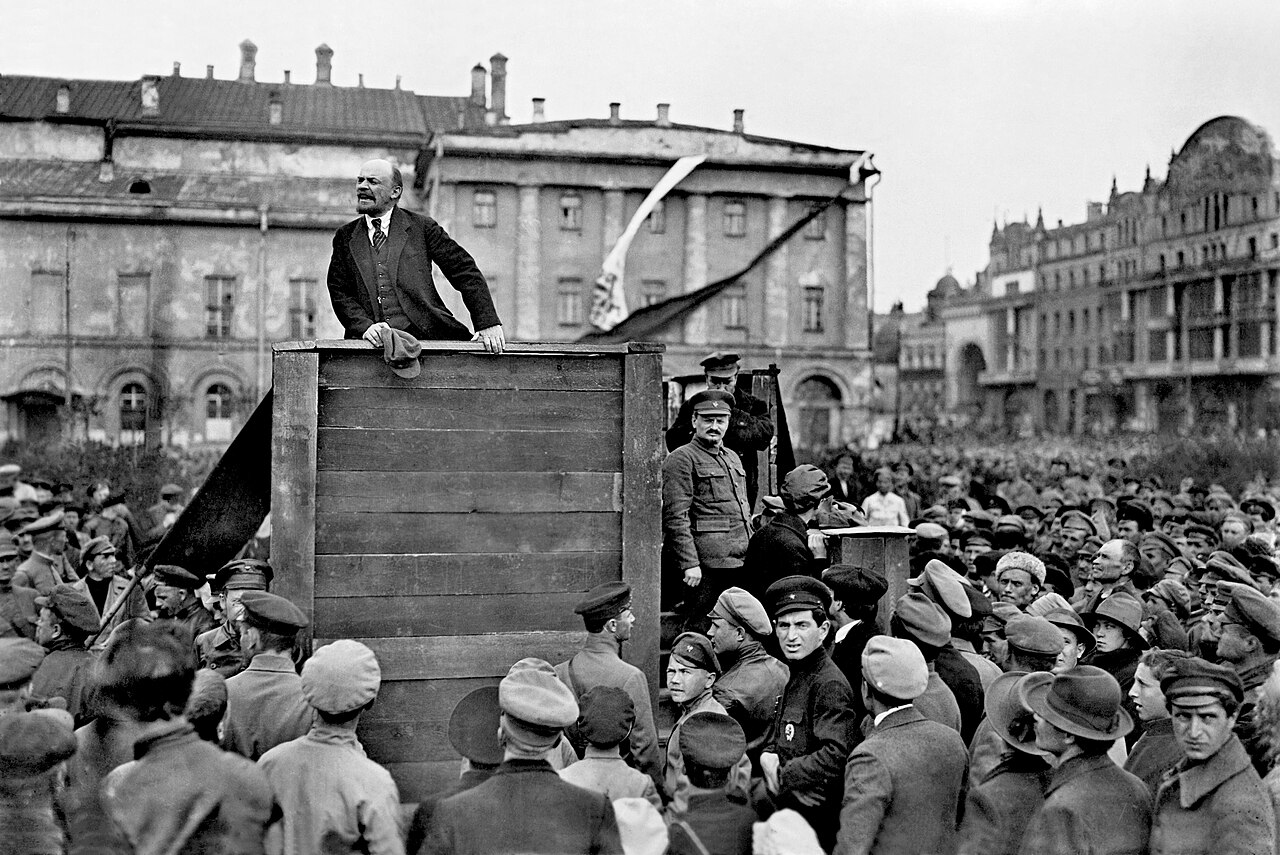 Lenin speaking from a wooden platform in Sverdlov Square, Moscow, 5 May 1920, with Trotsky and Kamenev on the steps at the right