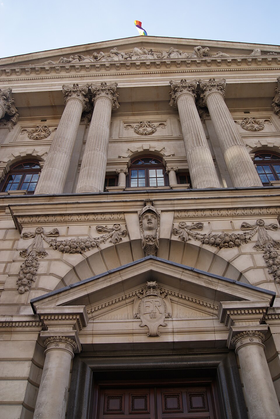 Upward view of a stone government building facade with Corinthian columns, a carved pediment and a doorway bearing the royal cypher ER VII