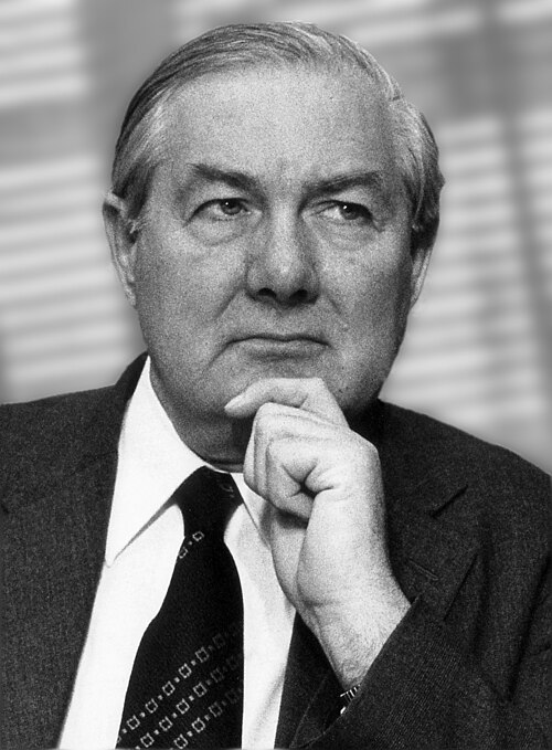 James Callaghan in a dark suit and patterned tie, chin resting on his hand