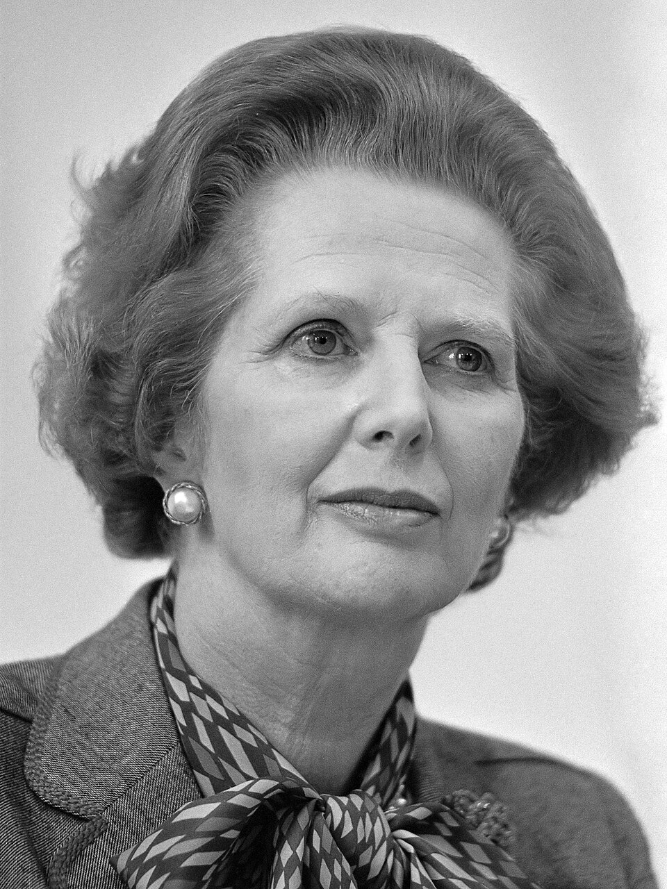 Margaret Thatcher in a black-and-white portrait, wearing a patterned scarf and pearl earring