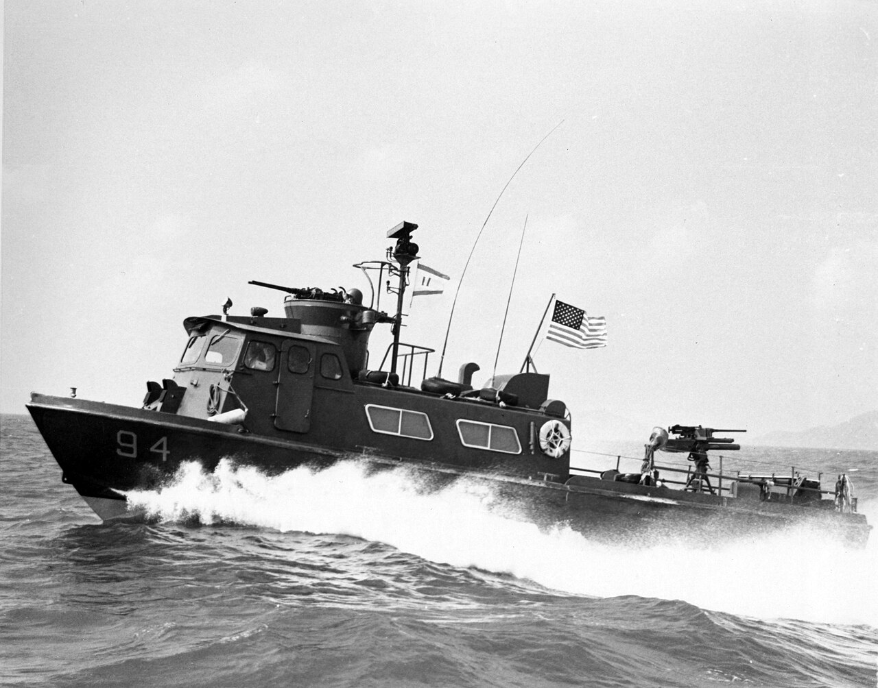 A U.S. Navy 50-foot Fast Patrol Craft with the hull number 94 on its bow throws up a wake at speed, a machine gun on its roof and a flag at its stern