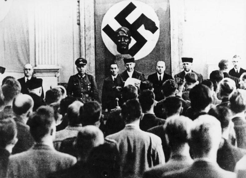 Roland Freisler reading a judgment during a Volksgerichtshof trial on the 20 July 1944 plot, with a bust and swastika banner behind him and spectators in the foreground