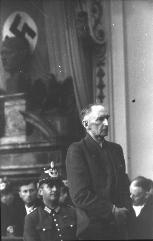 Field Marshal Erwin von Witzleben standing before the court, a guard beside him and a swastika banner behind