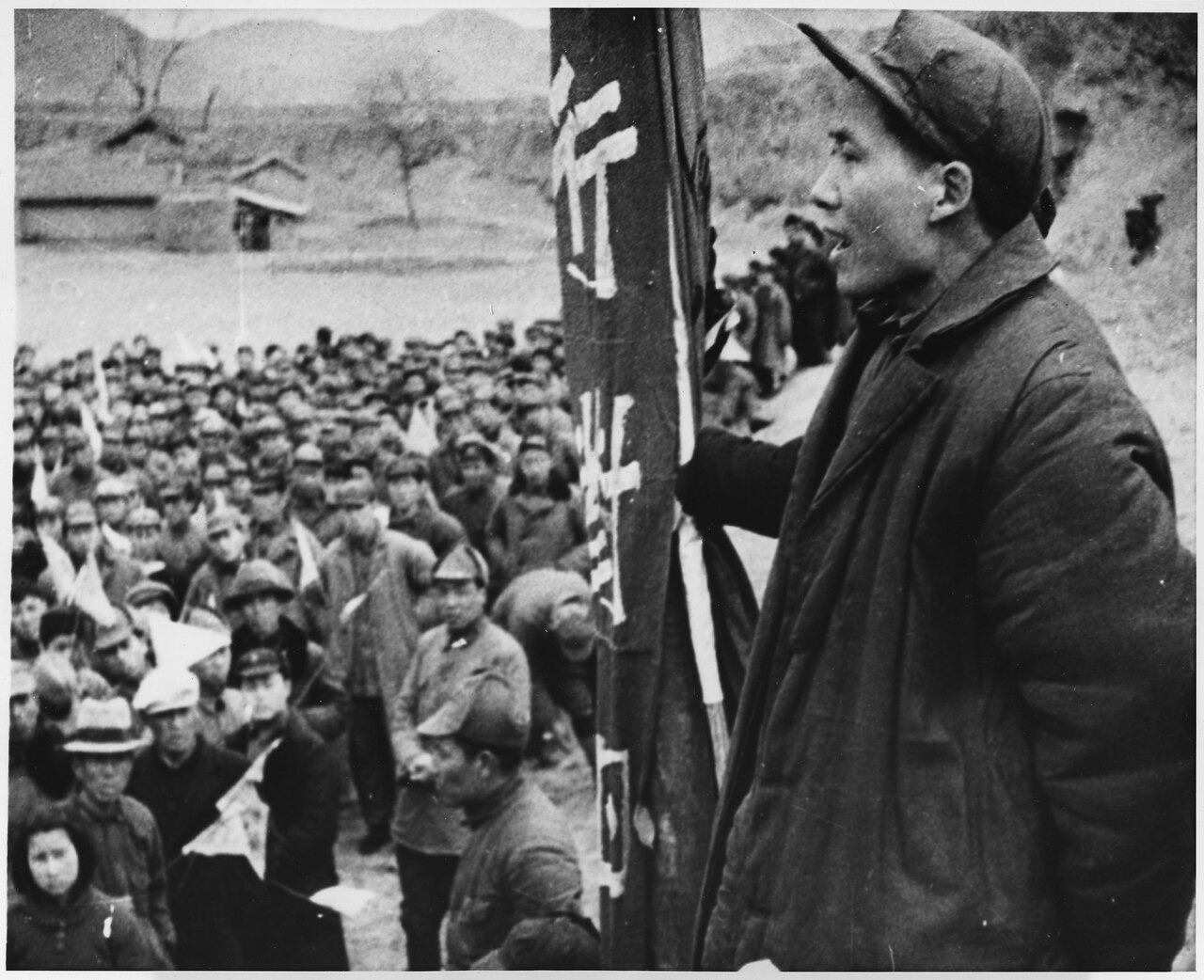 Mao Zedong addresses a crowd from a raised platform, holding a banner, at Yan'an, 6 December 1944