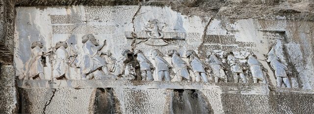 Behistun (Bisotun) rock relief and trilingual inscription of Darius I: the king, two attendants and the bound rebel leaders beneath the winged figure of Ahuramazda