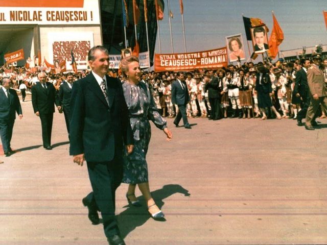 Nicolae and Elena Ceaușescu before a costumed crowd with portrait banners, 1986