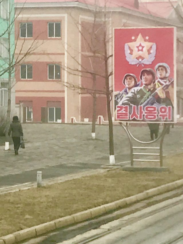 "결사옹위" (defend to the death): roadside sign with armed figures, North Korea (photographed 2017)