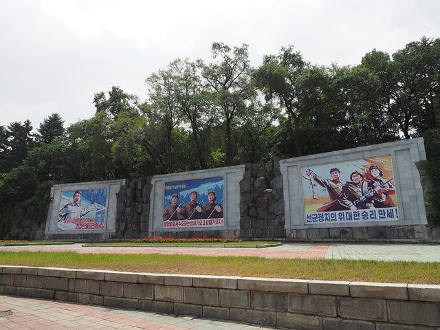 Three roadside murals: "Long live the great victory of Songun politics!" and two companion slogans, Pyongyang (photographed 2014)