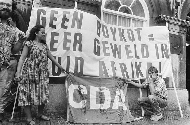 "Geen boykot = meer geweld in Zuid-Afrika" banner and stained CDA flag, The Hague (1983)