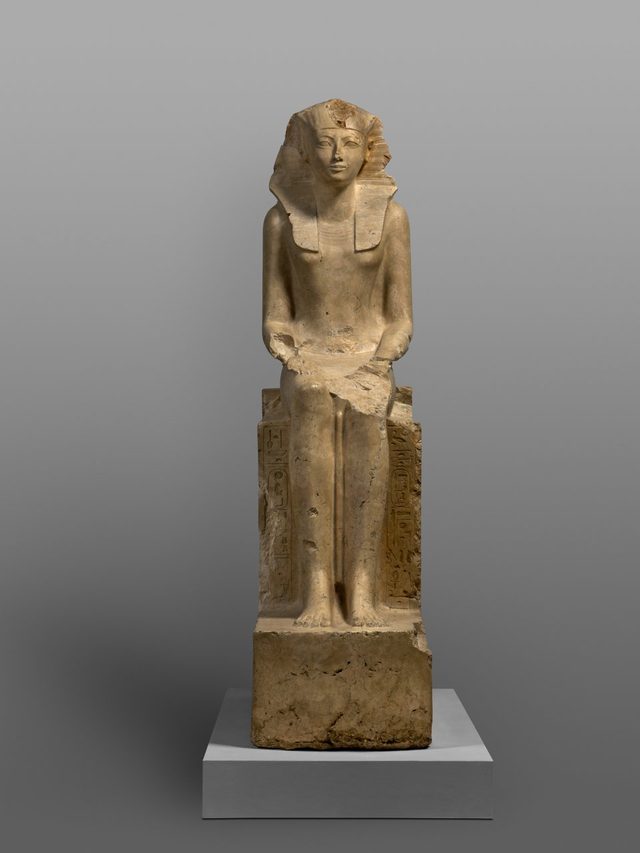 Seated limestone statue of Hatshepsut as king, with feminine royal titles on the throne, reassembled from fragments broken up at Deir el-Bahri