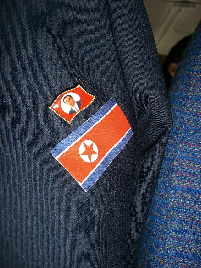 Kim Il-sung portrait flag pin beside a national flag patch, North Korea (photographed 2007)