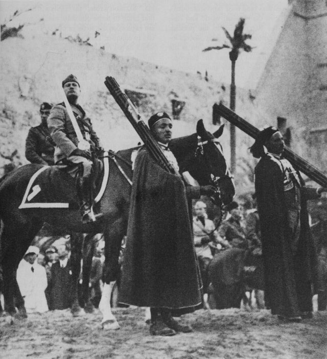 Mussolini on horseback with the 'Sword of Islam', flanked by two Libyan fasces-bearers, Tripoli, March 1937