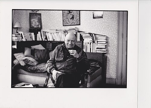 Jacques Ellul seated in an armchair in a room lined with books and stacked papers
