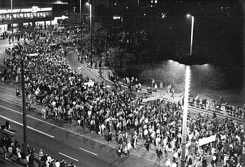 Black-and-white night photograph of a large crowd marching along a street in Leipzig during the Monday demonstration of 23 October 1989