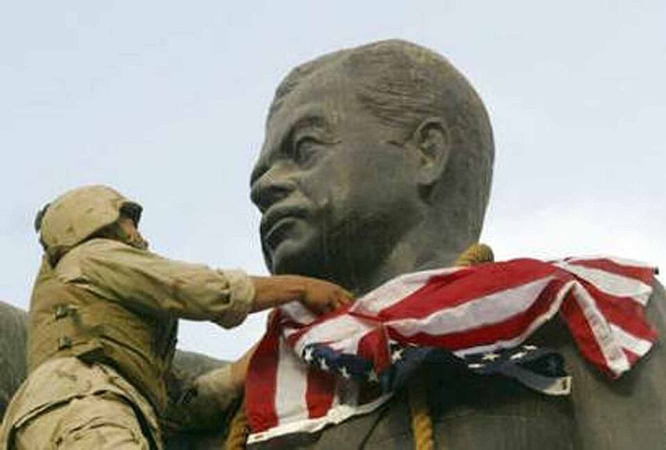 A US Marine drapes a US flag over the head of the statue of Saddam Hussein in Firdos Square, Baghdad