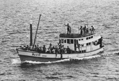 A Thai fishing boat crowded with people on deck, seen from above on open water