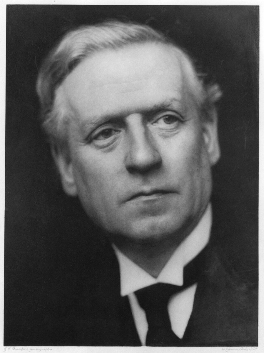 Head-and-shoulders studio portrait of a clean-shaven middle-aged man in a dark suit and high collar, looking to one side