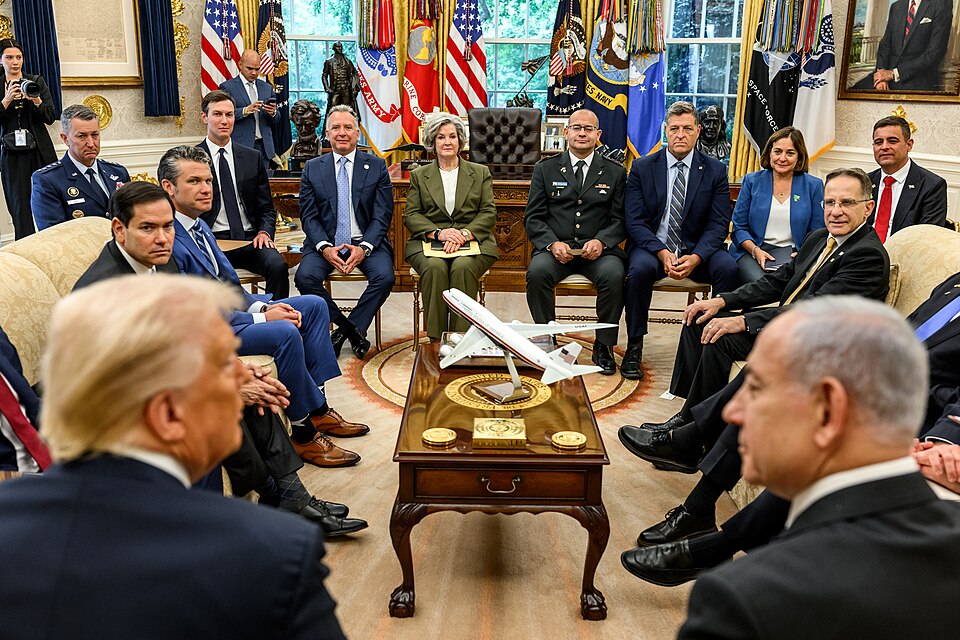 A meeting in the Oval Office: President Trump seated at left and Benjamin Netanyahu at right, seen from behind, with aides and officials seated and standing around a coffee table