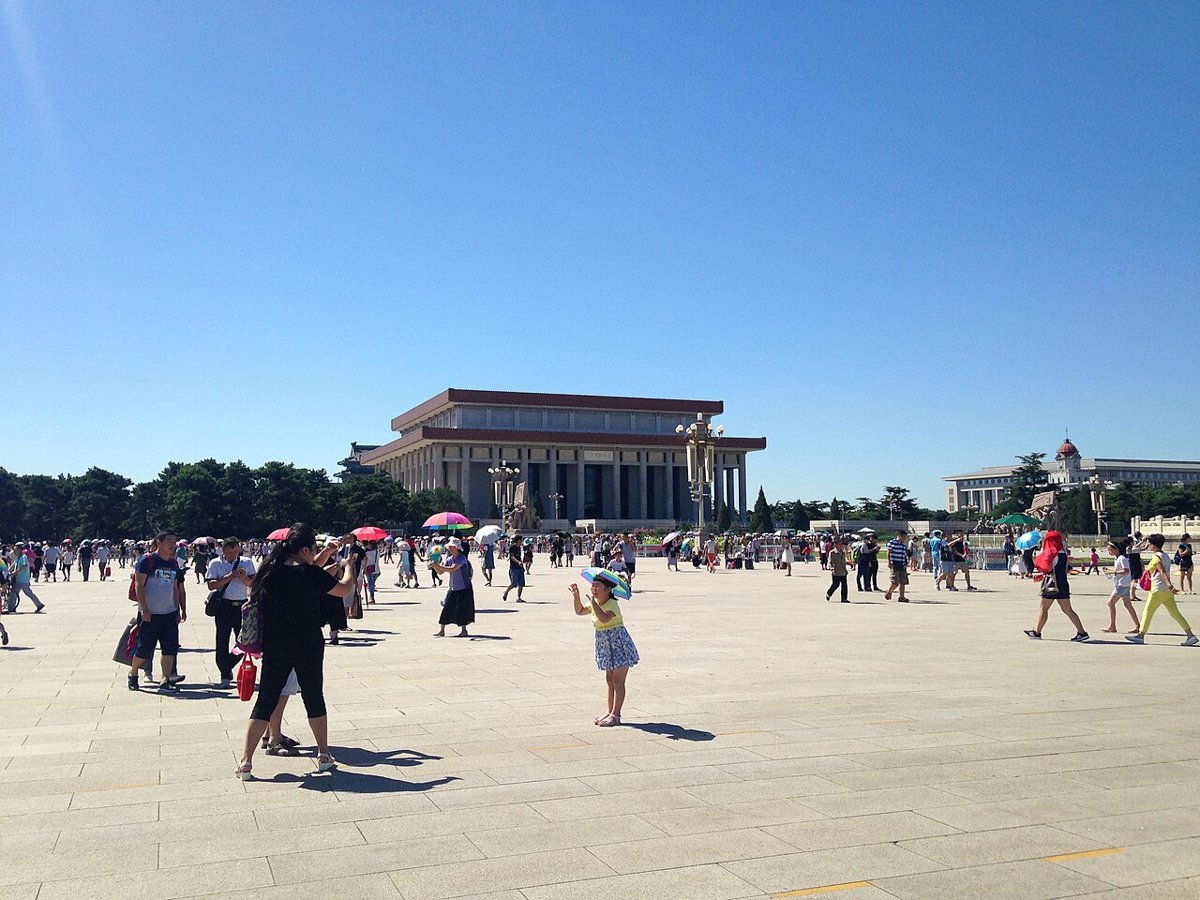 The low, colonnaded Chairman Mao Memorial Hall seen across a wide paved square on a clear day, with visitors in the foreground