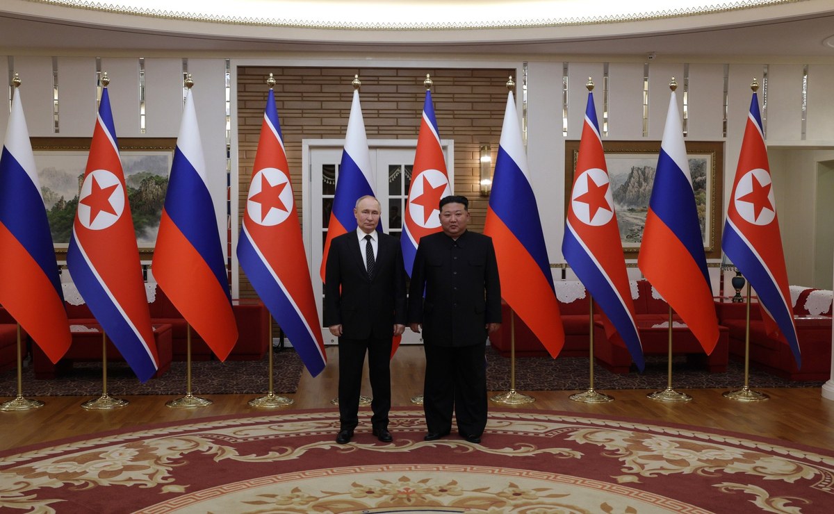 Vladimir Putin and Kim Jong Un standing side by side in front of rows of Russian and North Korean flags in Pyongyang