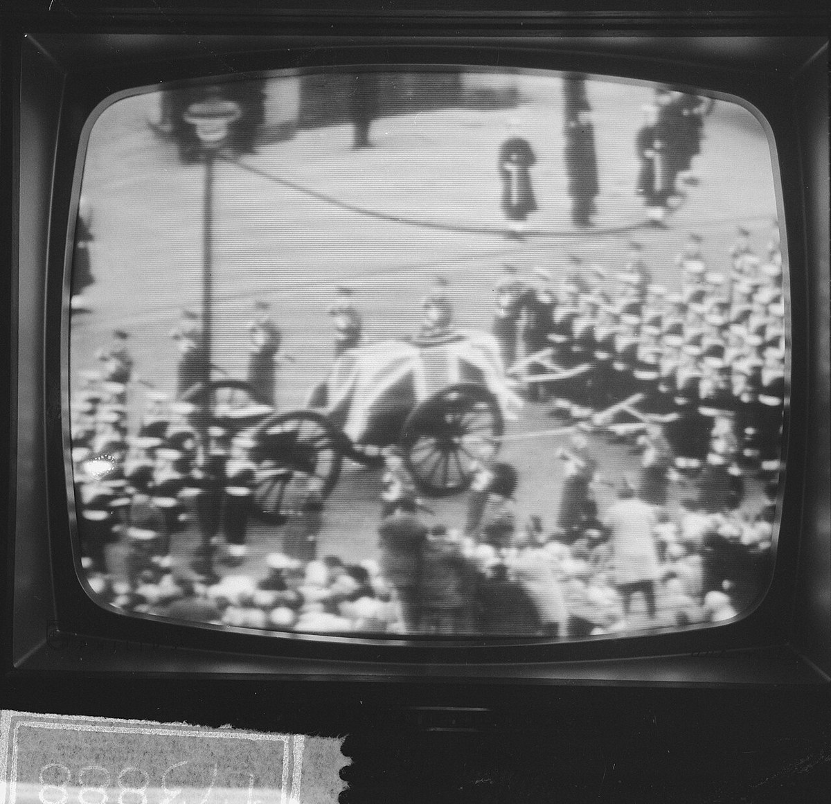 A television screen showing a flag-draped coffin on a gun carriage drawn by ranks of sailors through a crowd-lined London street