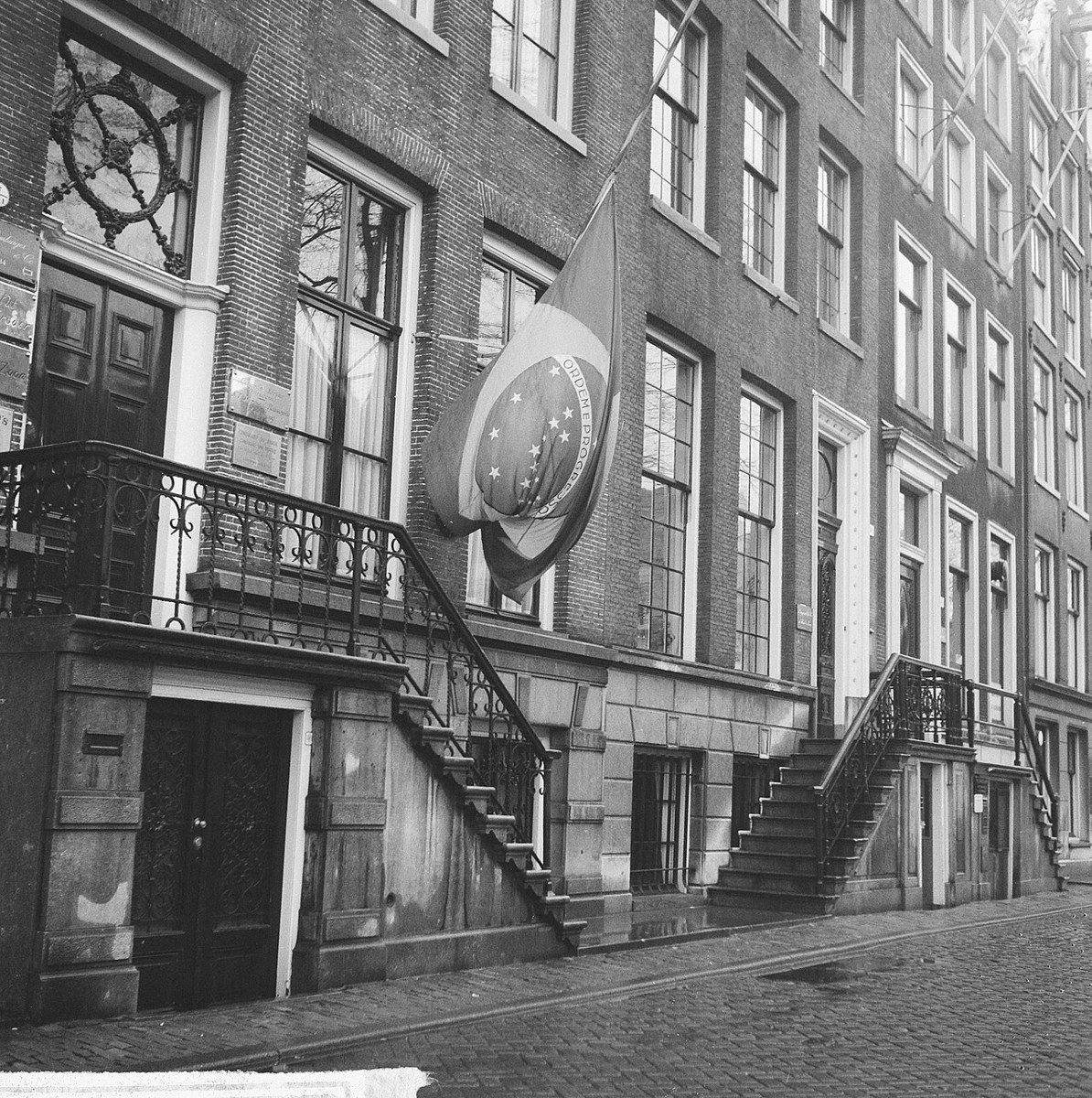 A flag at half-mast hanging from a brick canal house in Amsterdam, with the words Ordem e Progresso on its central disc