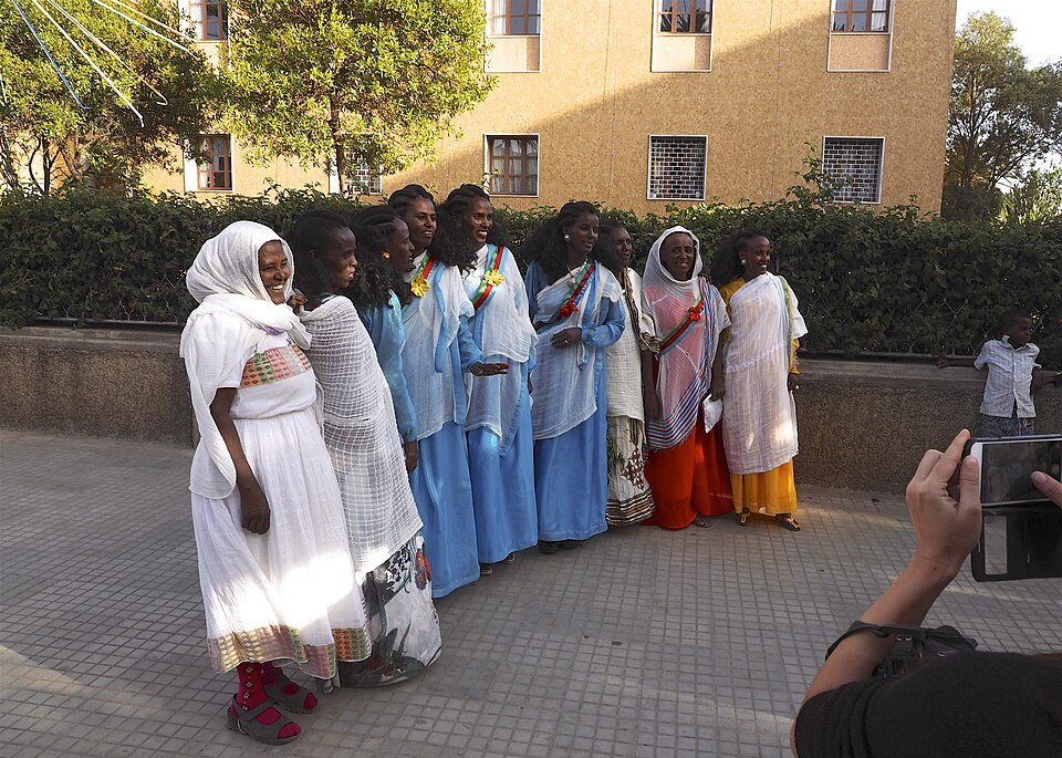 Eight women in white and coloured dresses with flag-coloured sashes pose for a photograph on a street in Asmara.