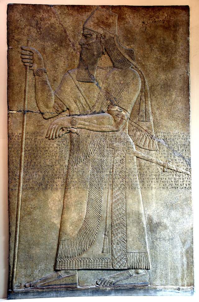 Ashurnasirpal II in a carved wall relief from Nimrud, standing in profile with a staff, in the British Museum